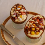 Cheesecake filled Easter eggs topped with chocolate chunks, chocolate sauce and Mini Eggs on a plate next to a knife
