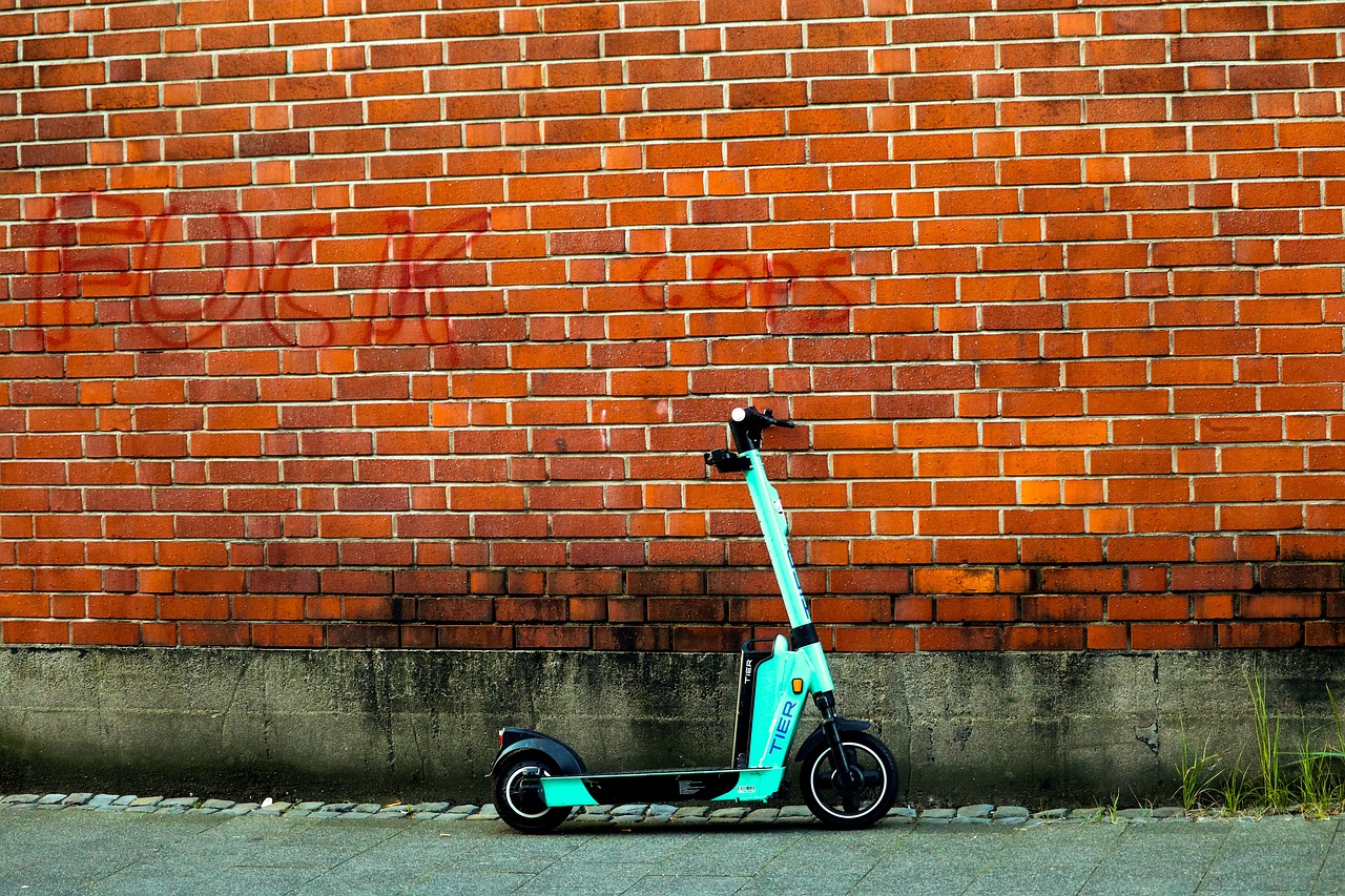 A mint green electric scooter propped up against a red brick wall