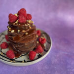 Chocolate protein pancakes topped with raspberries and chocolate sauce