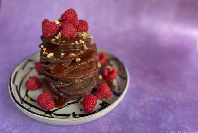 Chocolate protein pancakes topped with raspberries and chocolate sauce