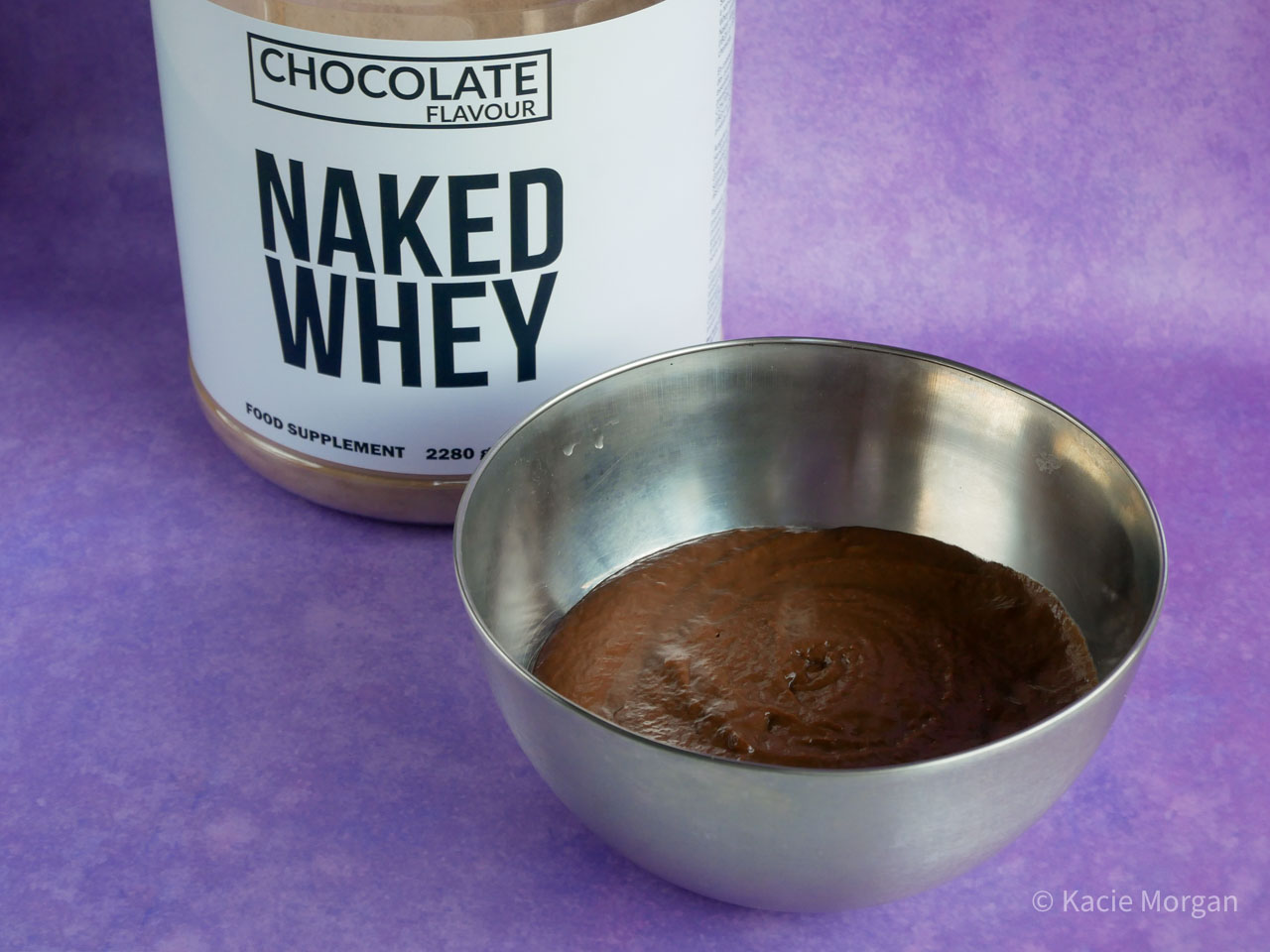 Batter mix for chocolate protein pancakes, next to a tub of Naked Nutrition's chocolate whey protein powder
