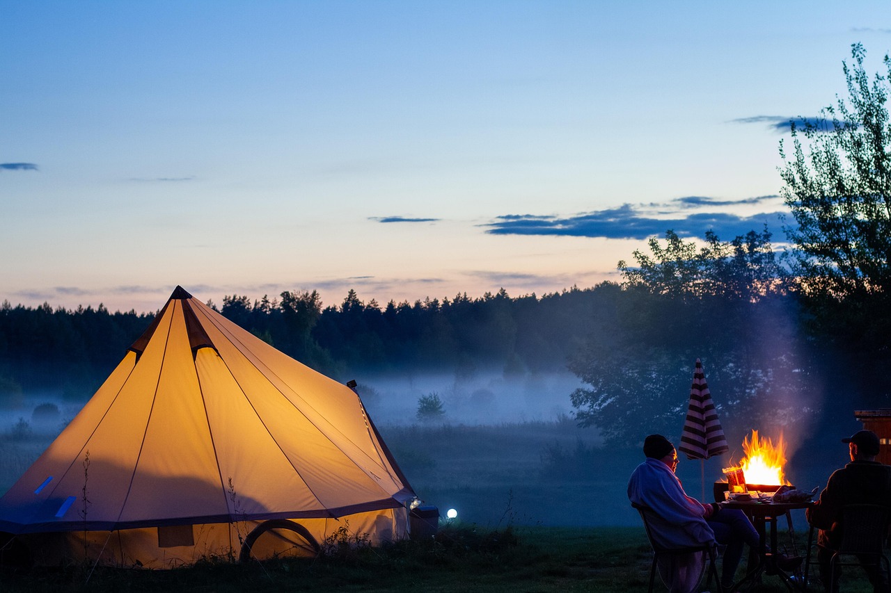 A glamping tent pictured at dusk, next to a campfire.
