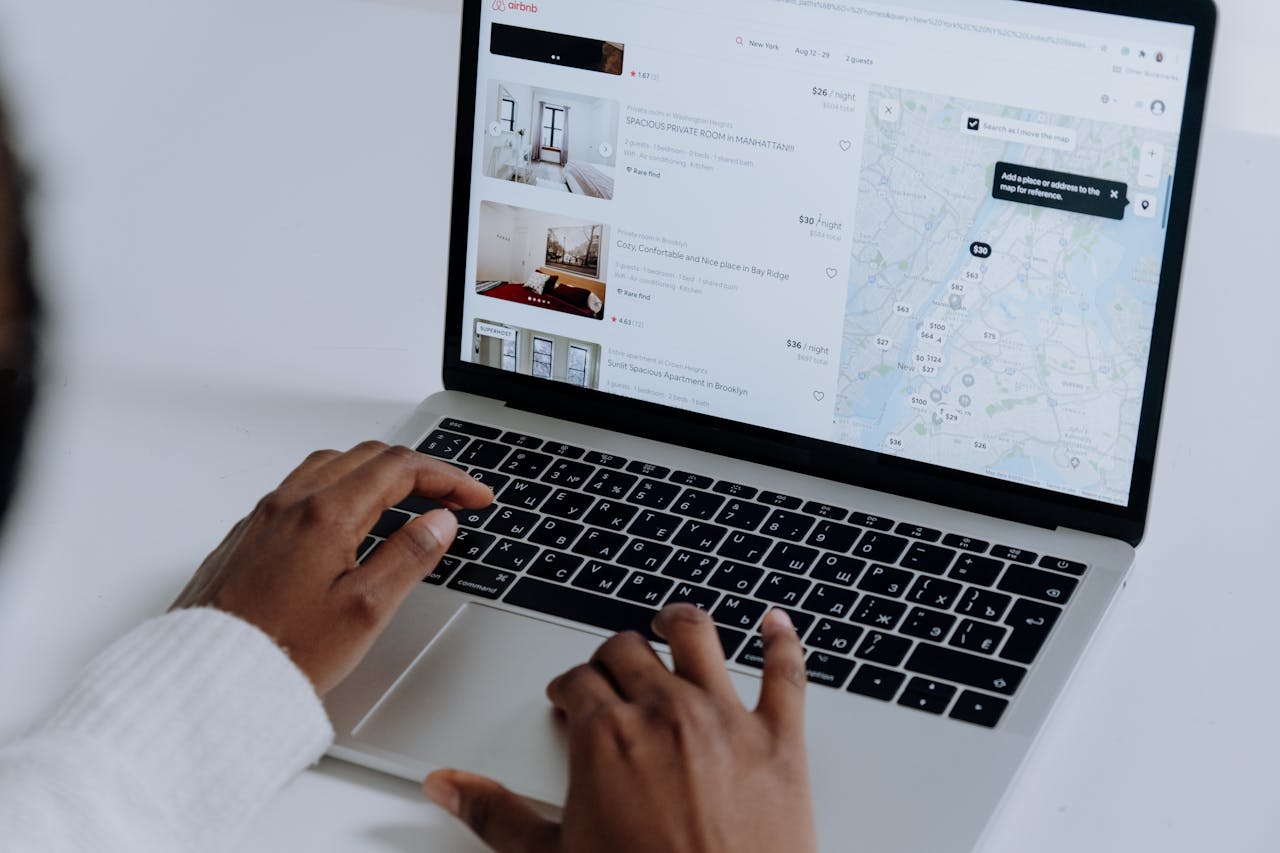 An over-shoulder shot of someone using a laptop to search accommodation bookings, with a map visible on the screen.