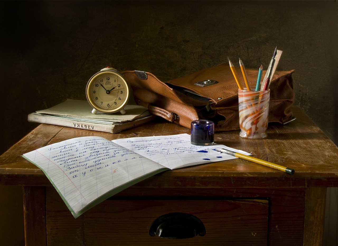 Schoolwork arranged on a table, next to a clock