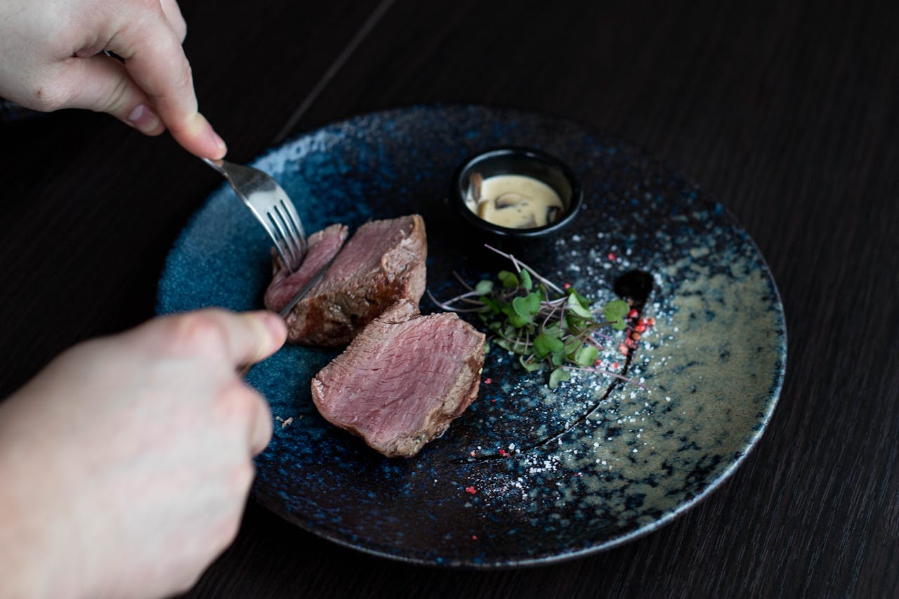 Grilled meat on a plate, being cut with a knife and fork