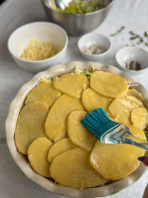 Basting the final layer of potato slices with butter, before putting the onion cake into the oven
