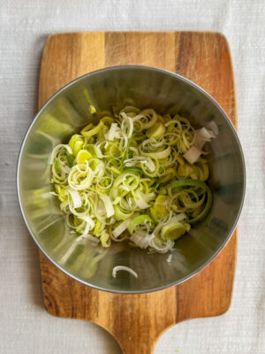 A bowl of finely sliced leeks sitting on a chopping board