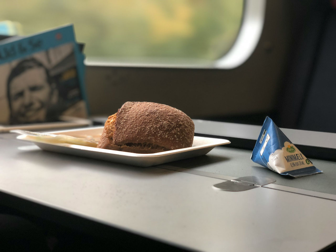 A bread roll and a milk carton on a food tray on-board a plane.