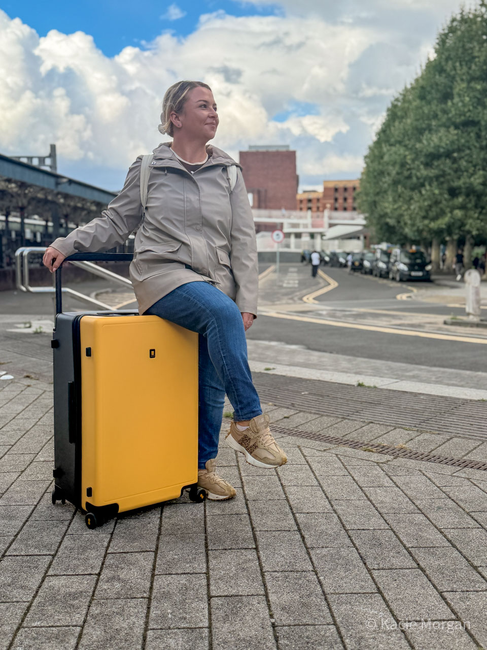 Kacie sitting on her suitcase smiling