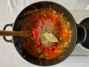 Add the chopped tomatoes to the pan along with the bay leaf, fresh rosemary, dried oregano, lamb stock, Worcestershire sauce, salt, and pepper.
