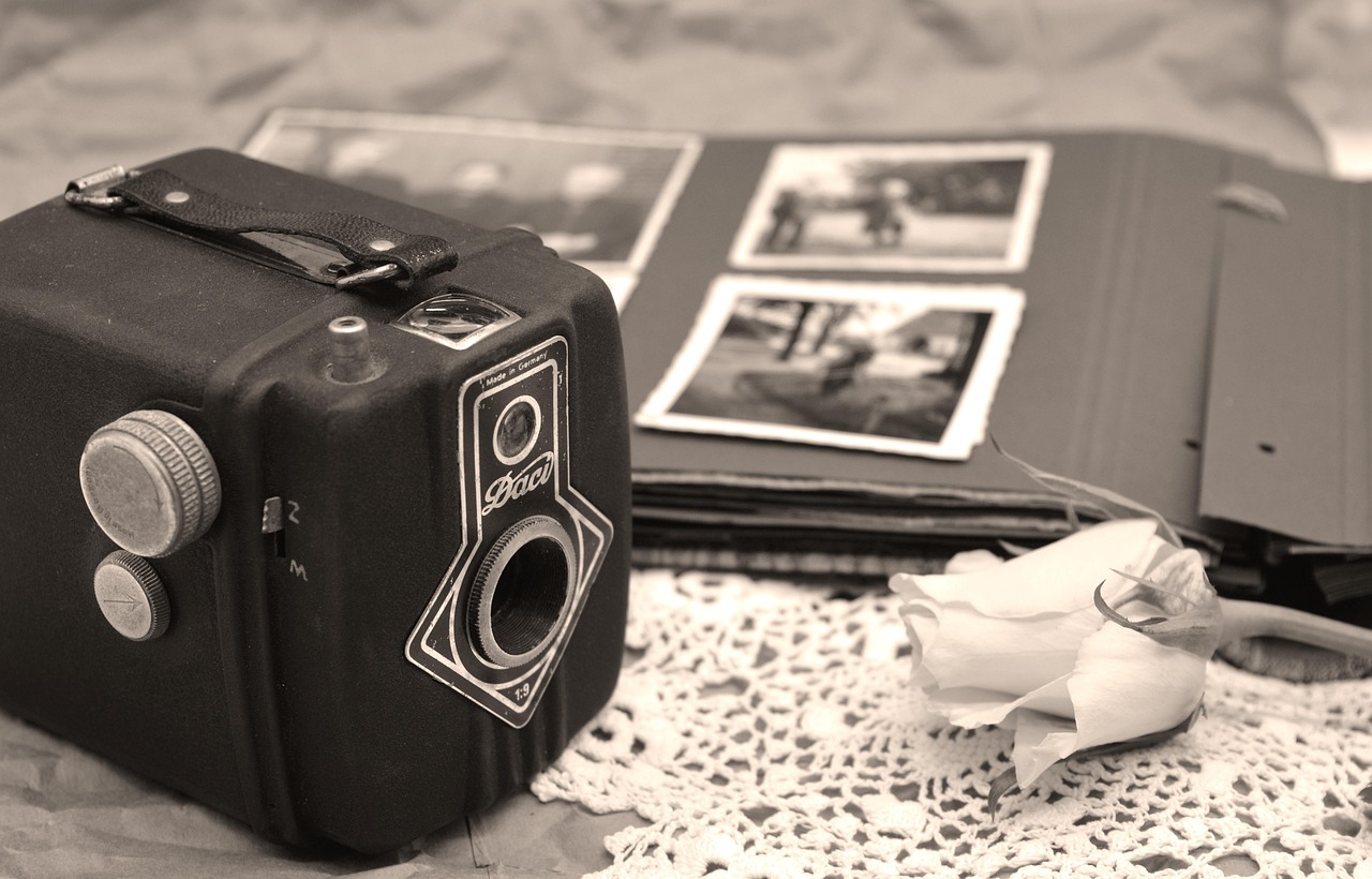 An old camea resting on a table next to an old photo album and a rose.
