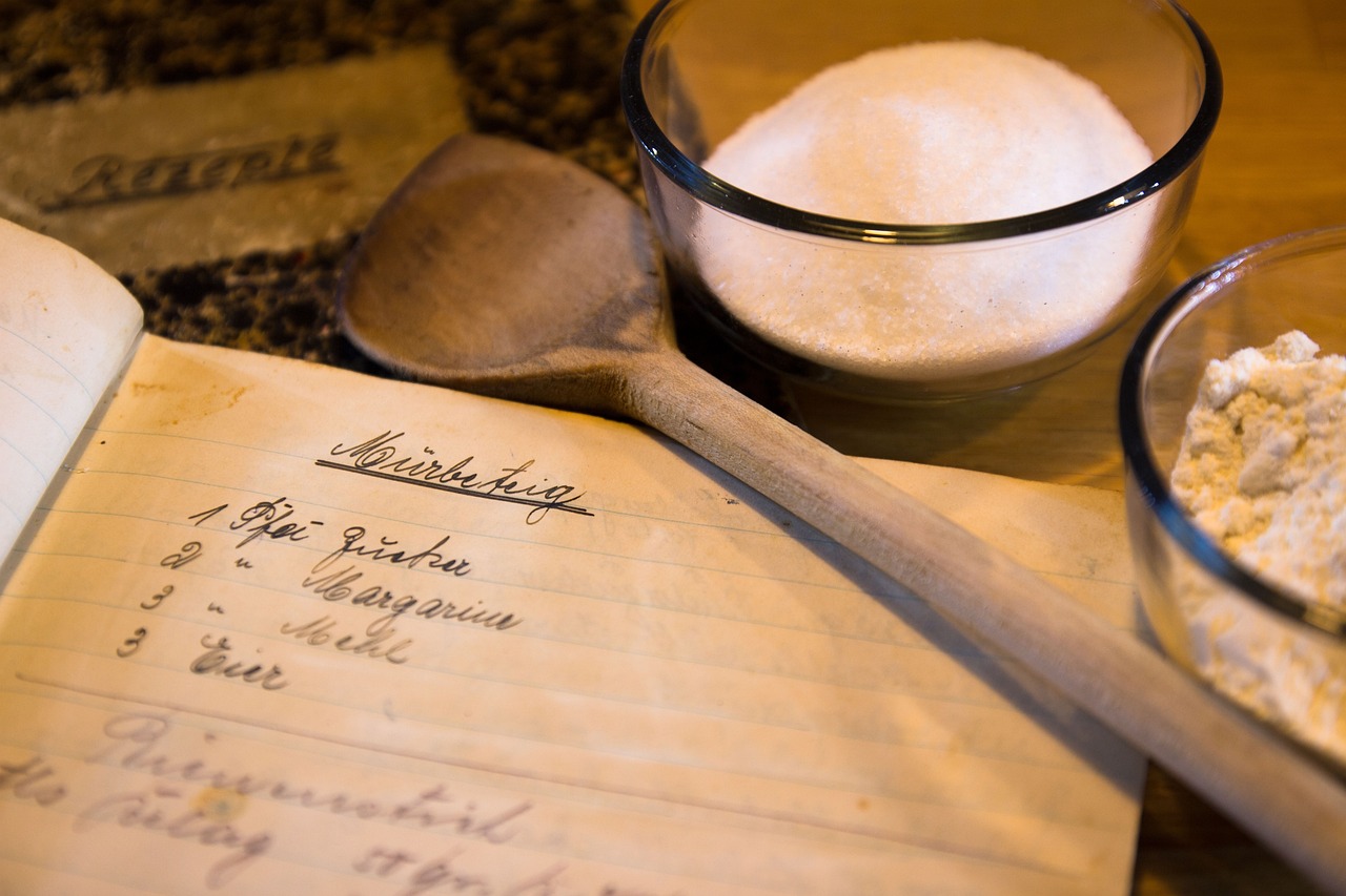 Bowl of sugar and wooden spoon next to a handwritten cookbook