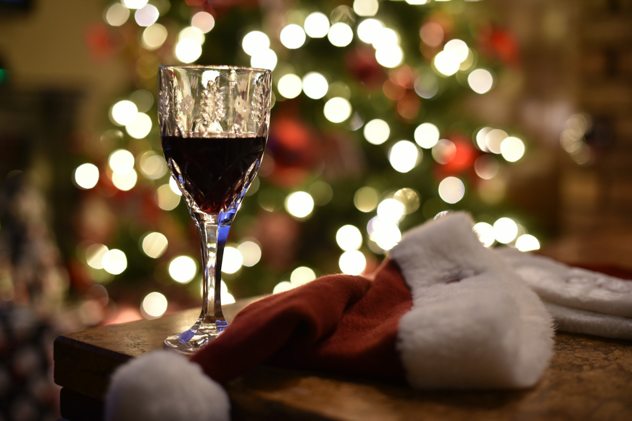 A glass of red wine and a Santa Claus hat on a table, with a Christmas tree in the background.